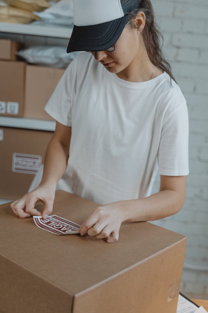 Woman preparing shipment by applying a fragile sticker on a cardboard box in a warehouse.